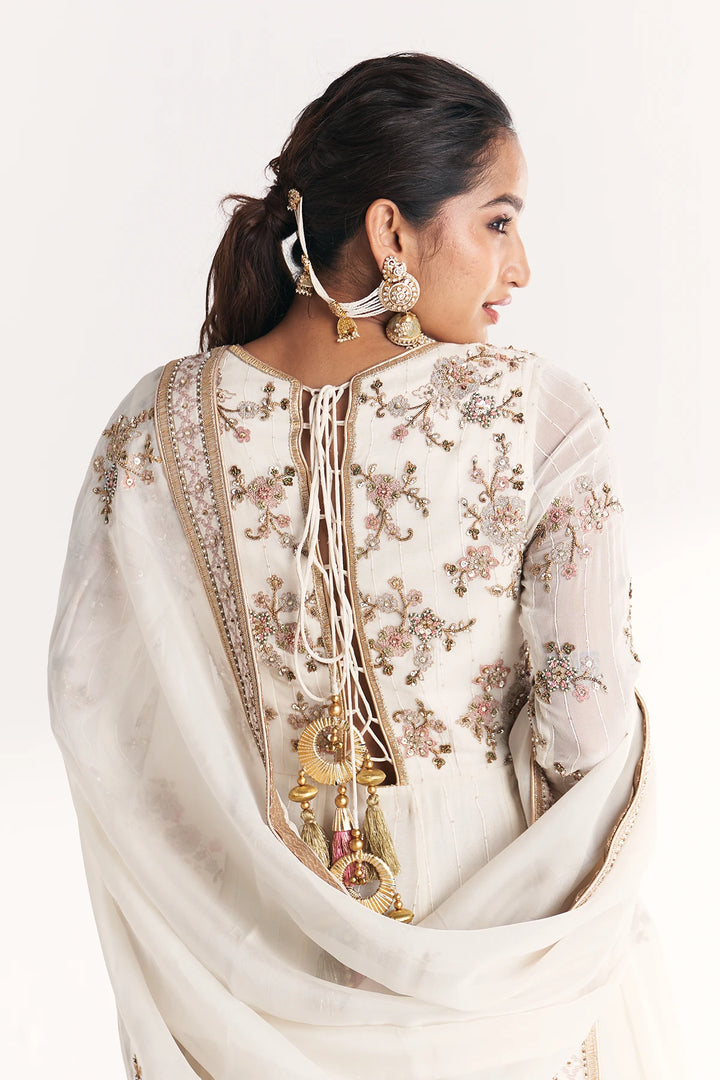 Woman wearing a white embroidered Anarkali with a plain background