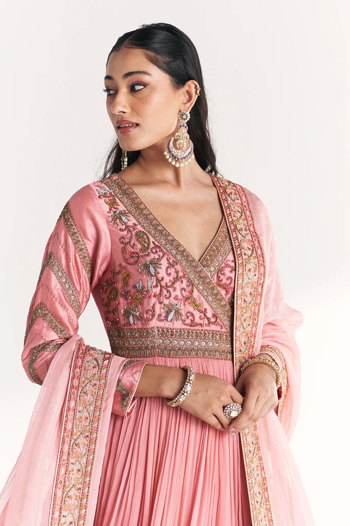 Woman wearing a pink traditional Anarkali with intricate embroidery on a white background