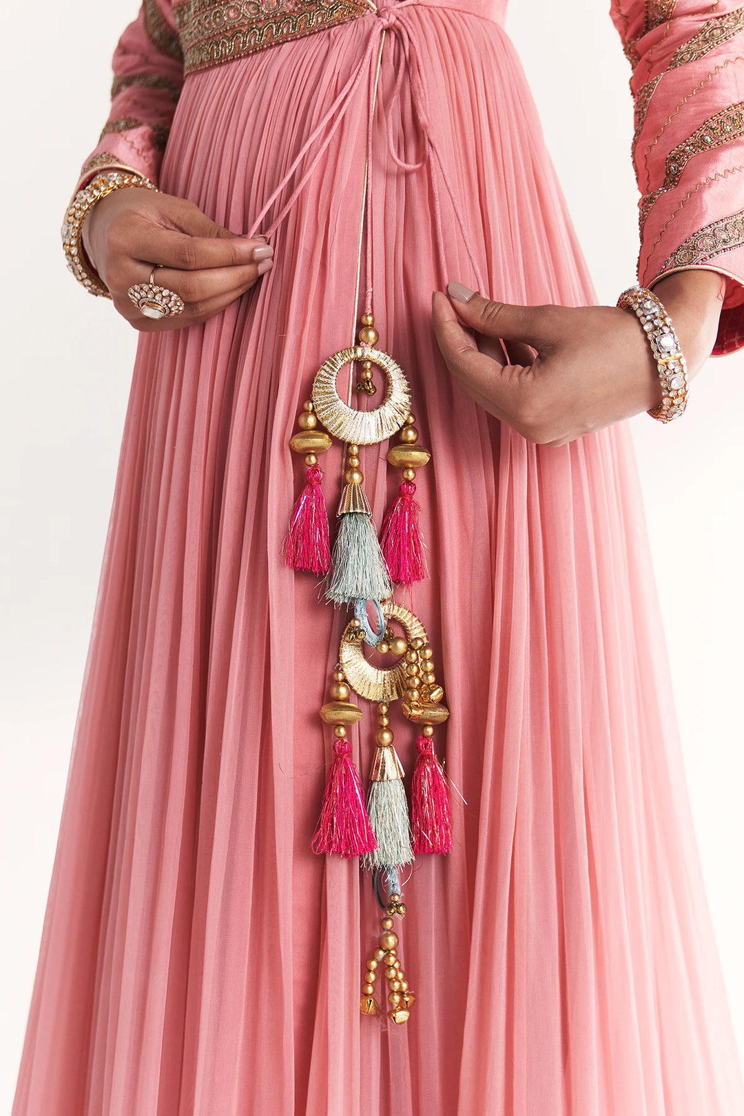 Person wearing a pink Anarkali with decorative jewelry and tassels.