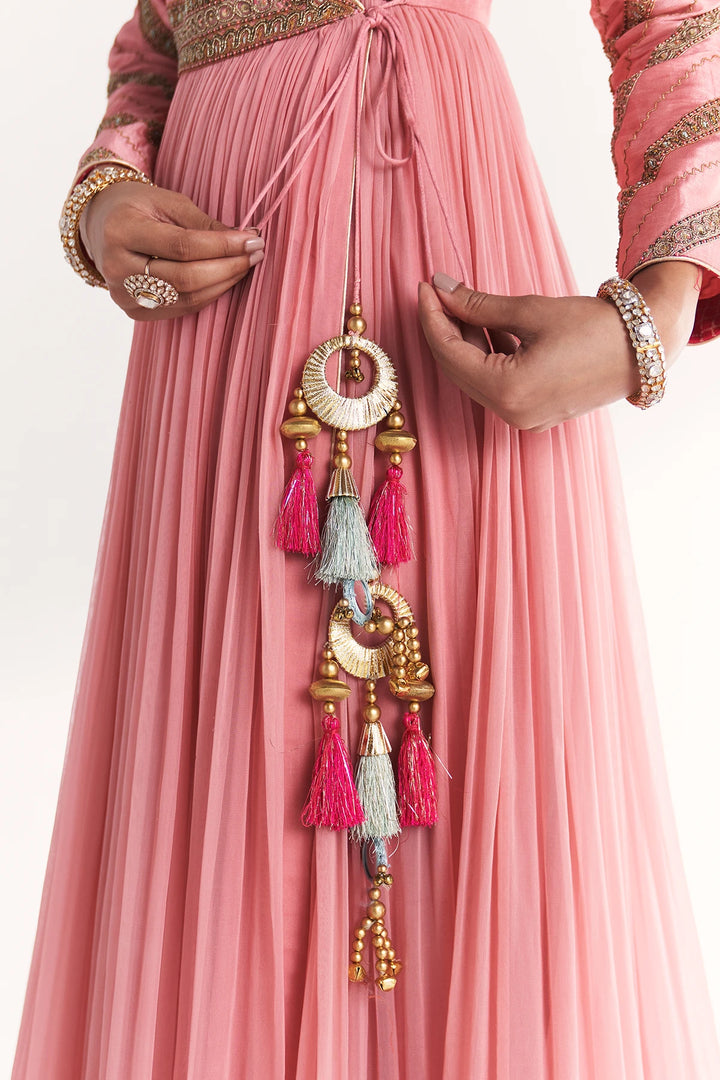 Person wearing a pink Anarkali with decorative jewelry and tassels.