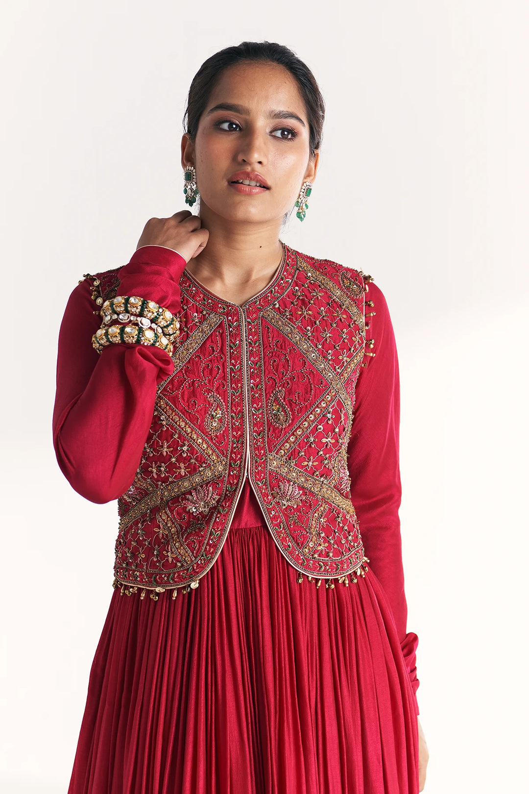 Woman wearing a red traditional Anarkali with intricate gold embroidery on a white background