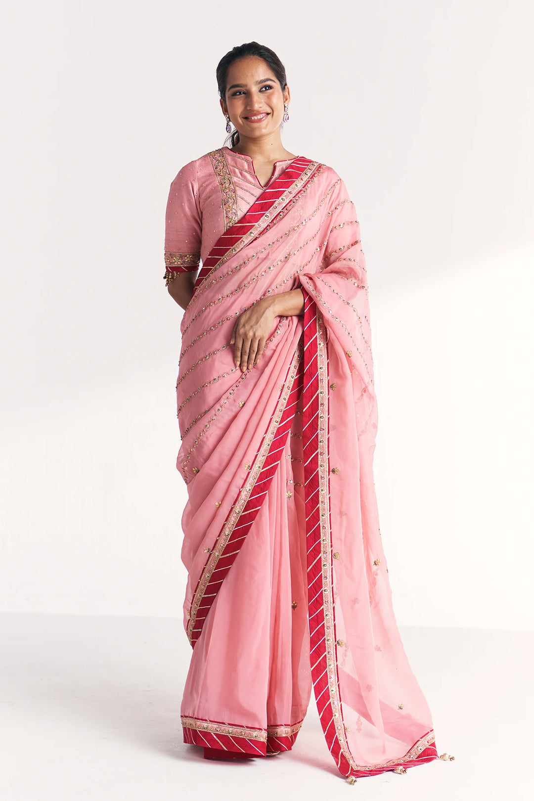 Woman wearing a pink saree with red and gold border on a white background