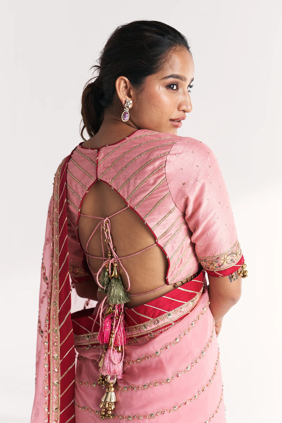 Woman wearing a pink saree with a backless design on a white background