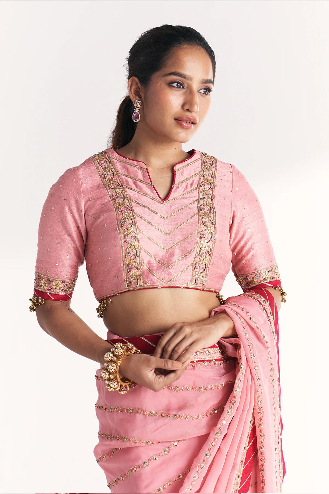 Woman wearing a pink saree with gold embroidery on a white background