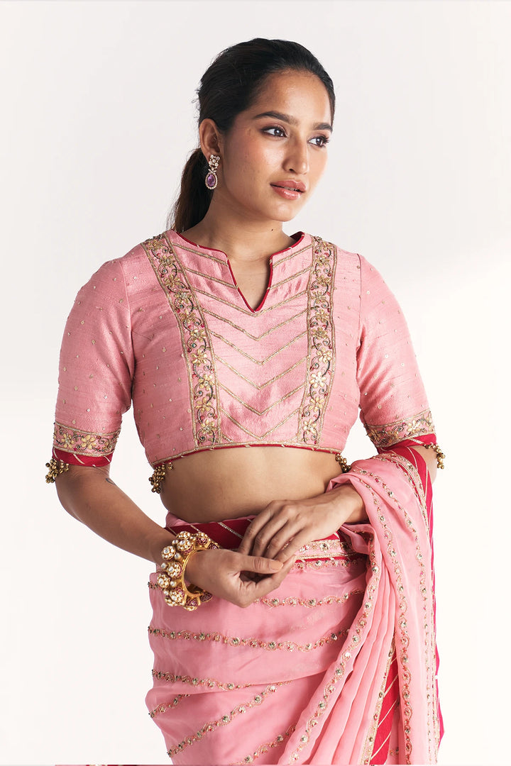 Woman wearing a pink saree with gold embroidery on a white background