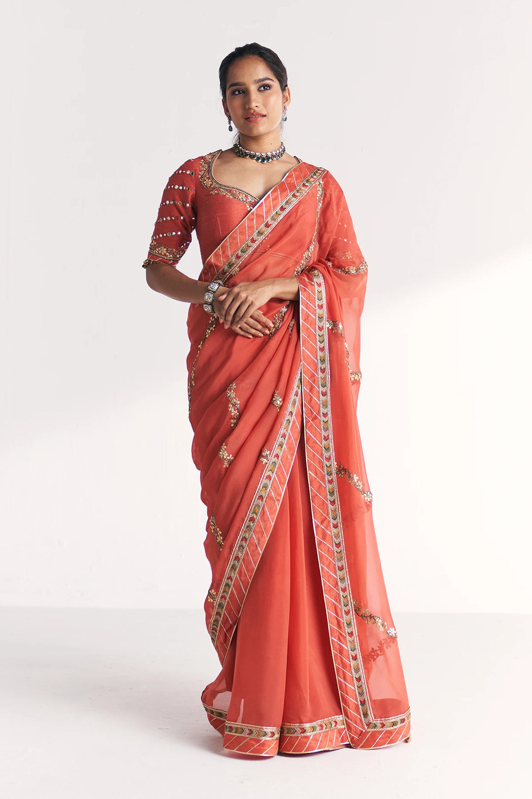 Woman wearing a traditional orange saree with intricate patterns on a white background
