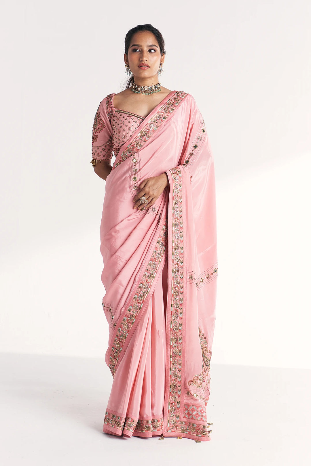 Woman wearing a pink saree with intricate designs on a white background