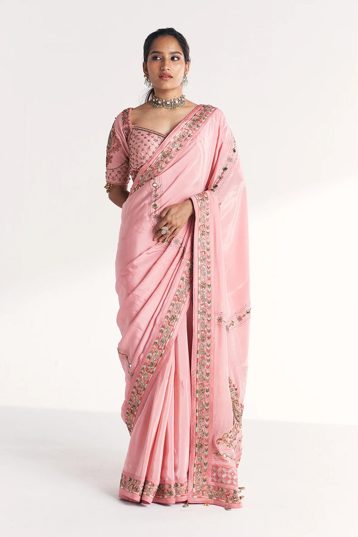 Woman wearing a pink saree with intricate designs on a white background