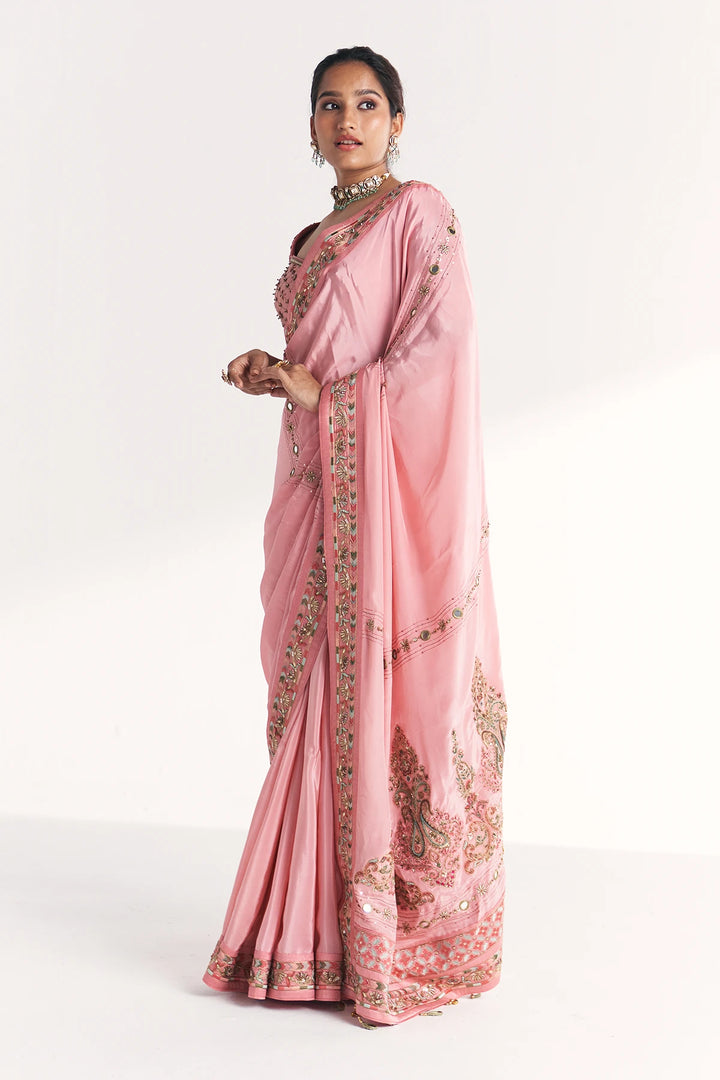 Woman wearing a pink saree with intricate designs on a white background
