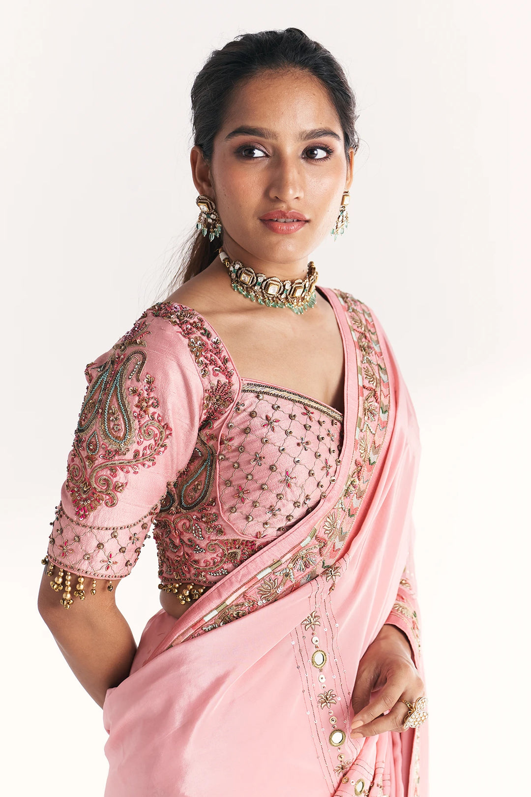 Woman wearing a pink saree with intricate designs on a white background