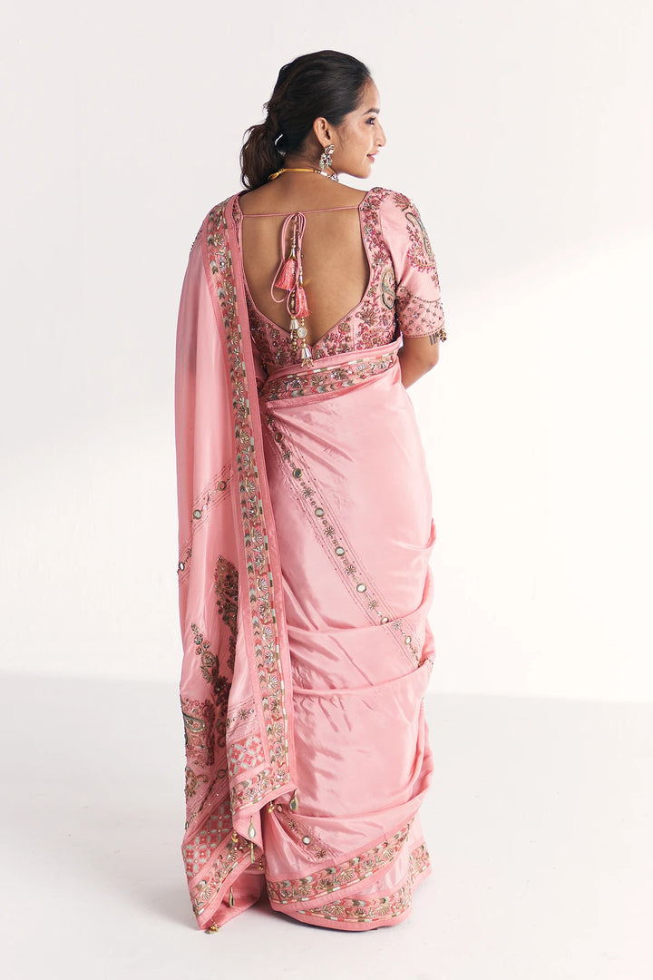 Woman wearing a pink saree with intricate designs on a white background