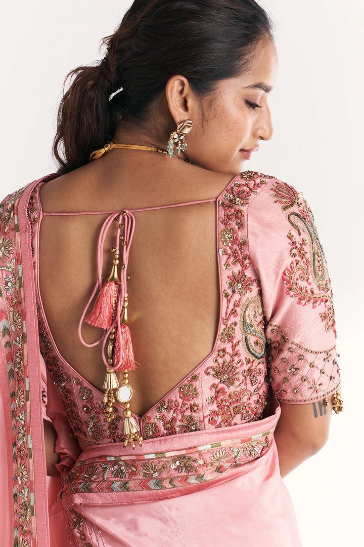 Woman wearing a pink embroidered blouse with a back design and tassels.