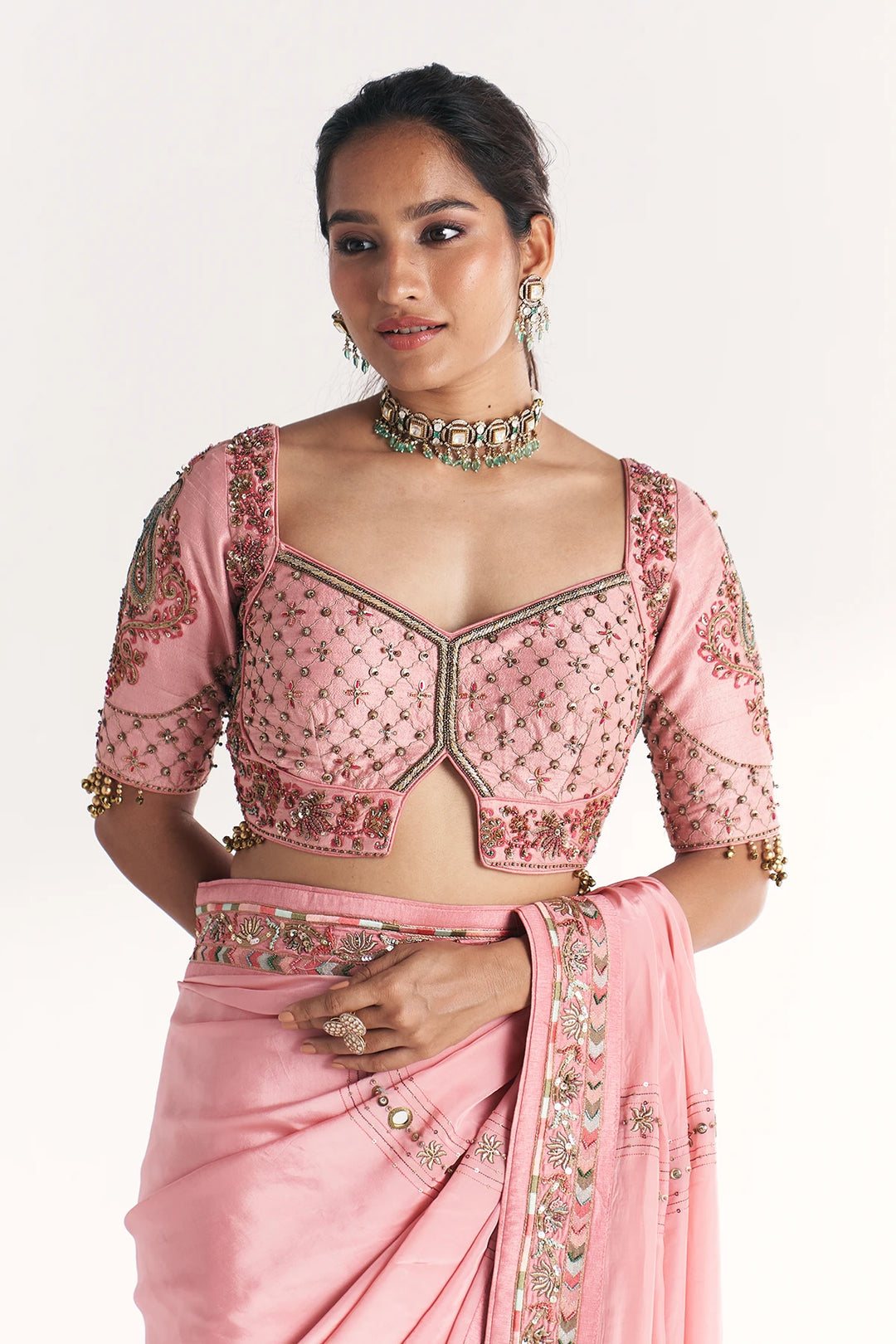Woman wearing a pink saree with intricate embroidery on a white background