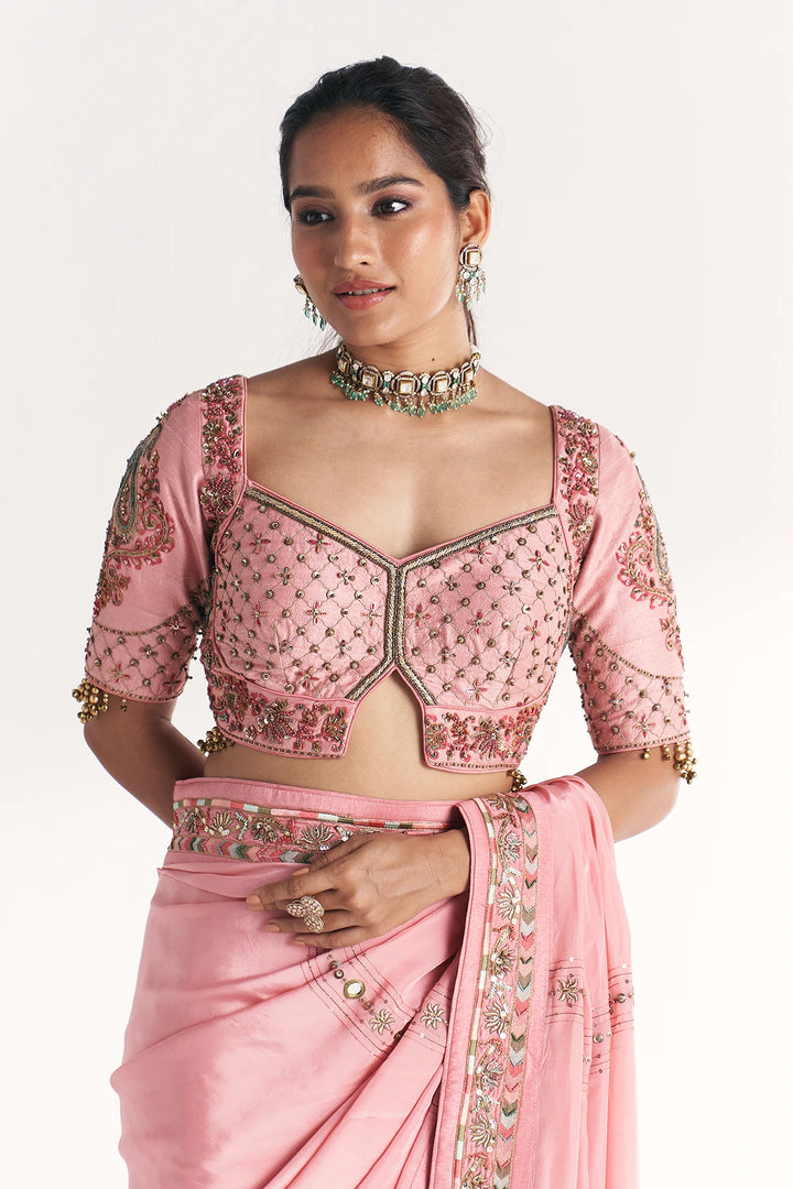 Woman wearing a pink saree with intricate embroidery on a white background