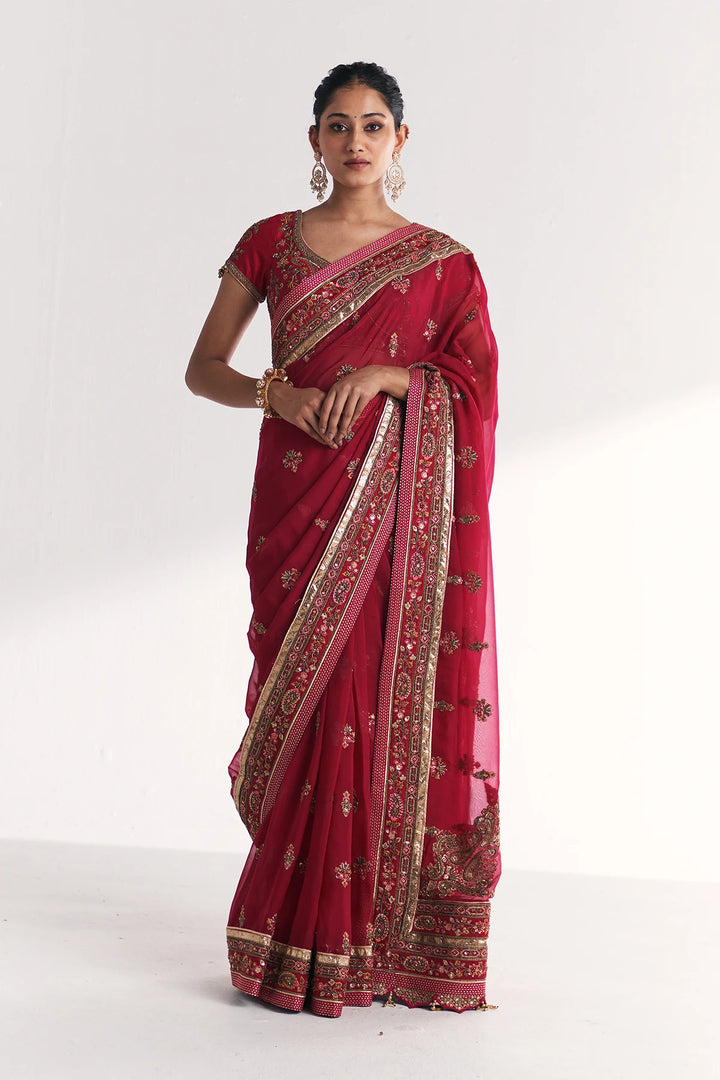 Woman wearing a red saree with gold patterns on a white background