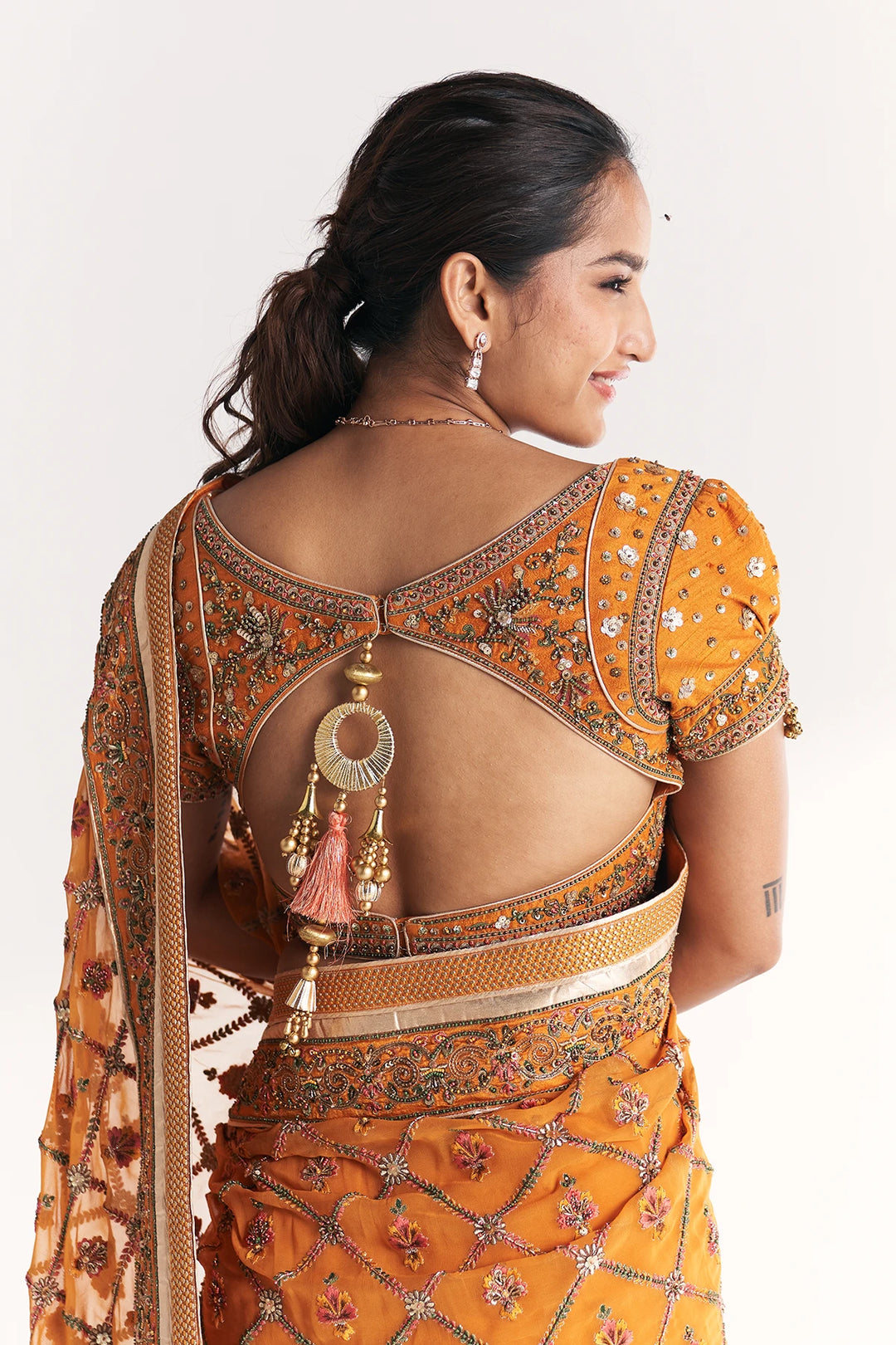 Woman wearing an orange embroidered saree with a plain background
