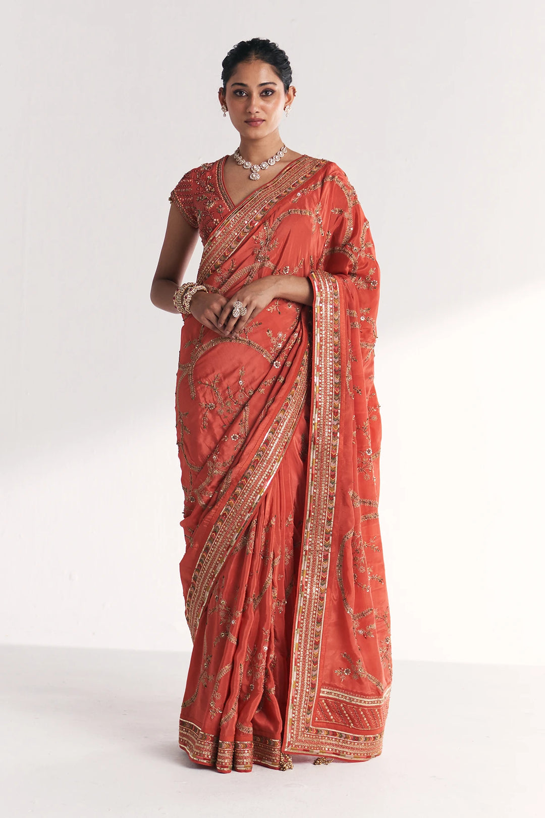 Woman wearing a traditional red saree with gold patterns on a white background