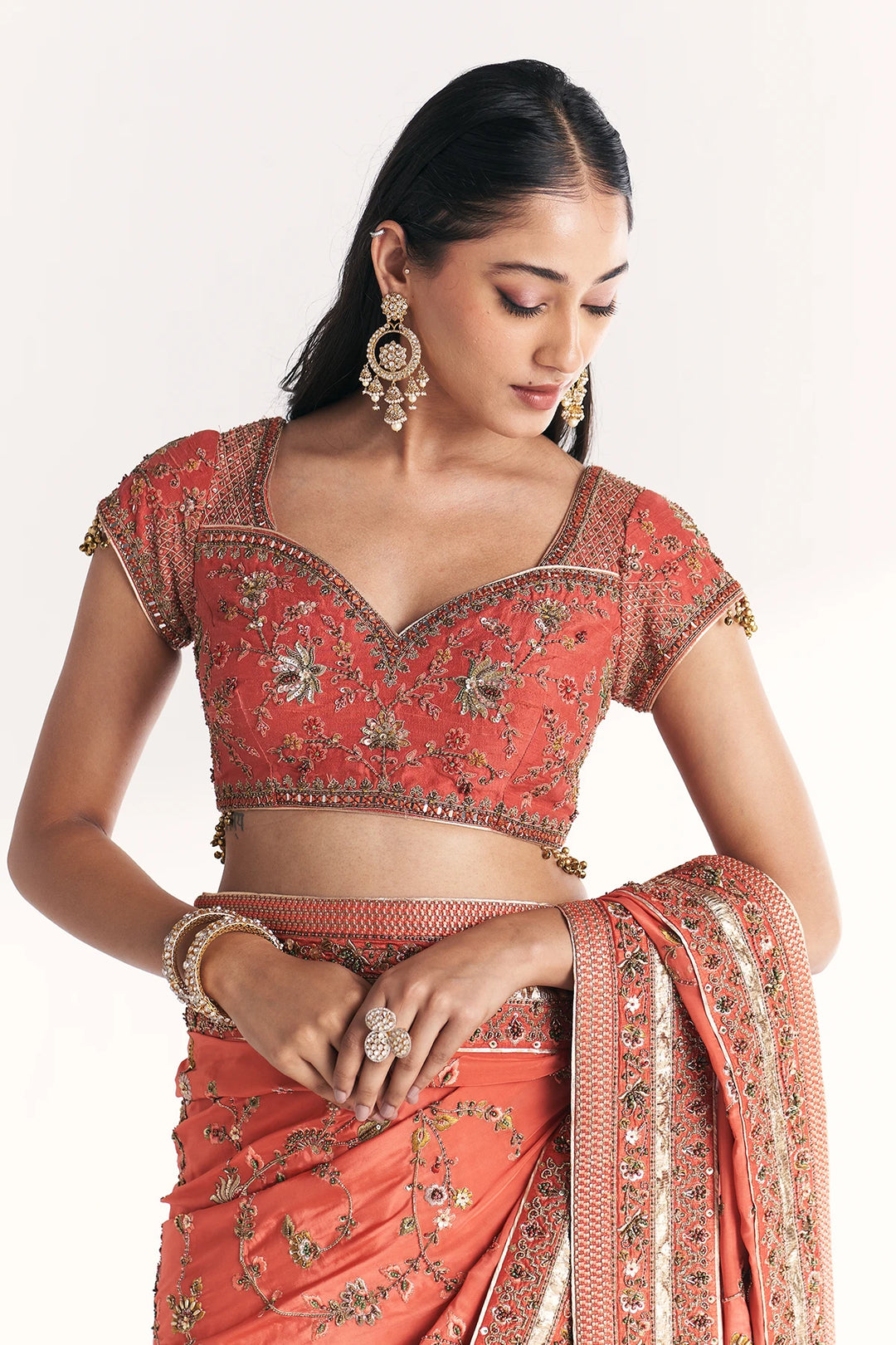 Woman wearing a traditional red and gold embroidered saree with blouse on a white background