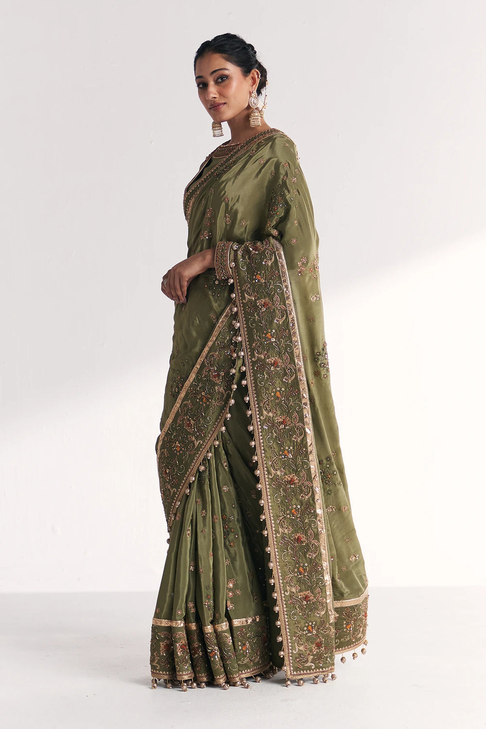 Woman wearing a green saree with intricate patterns on a white background