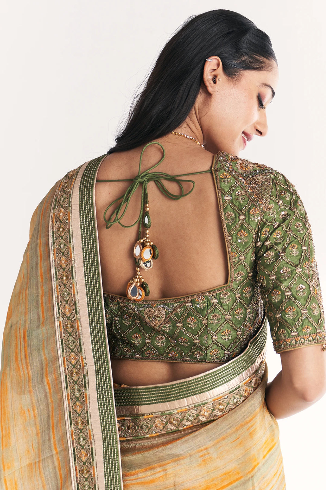 Woman wearing a green and beige saree with a decorative blouse on a white background