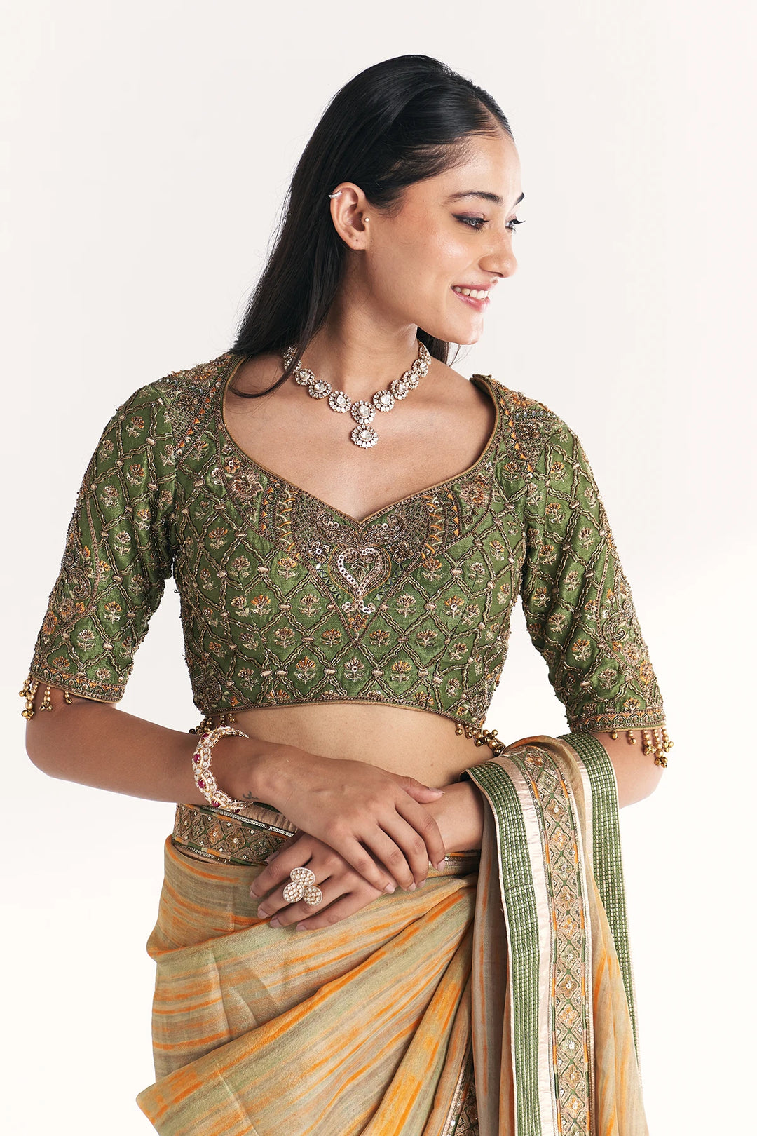 Woman wearing a green saree with a blouse, jewelry, and a plain background