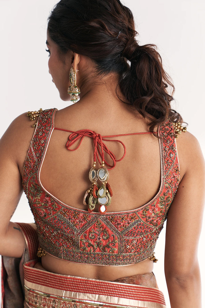Woman wearing a traditional embroidered blouse with intricate designs and gold jewelry.