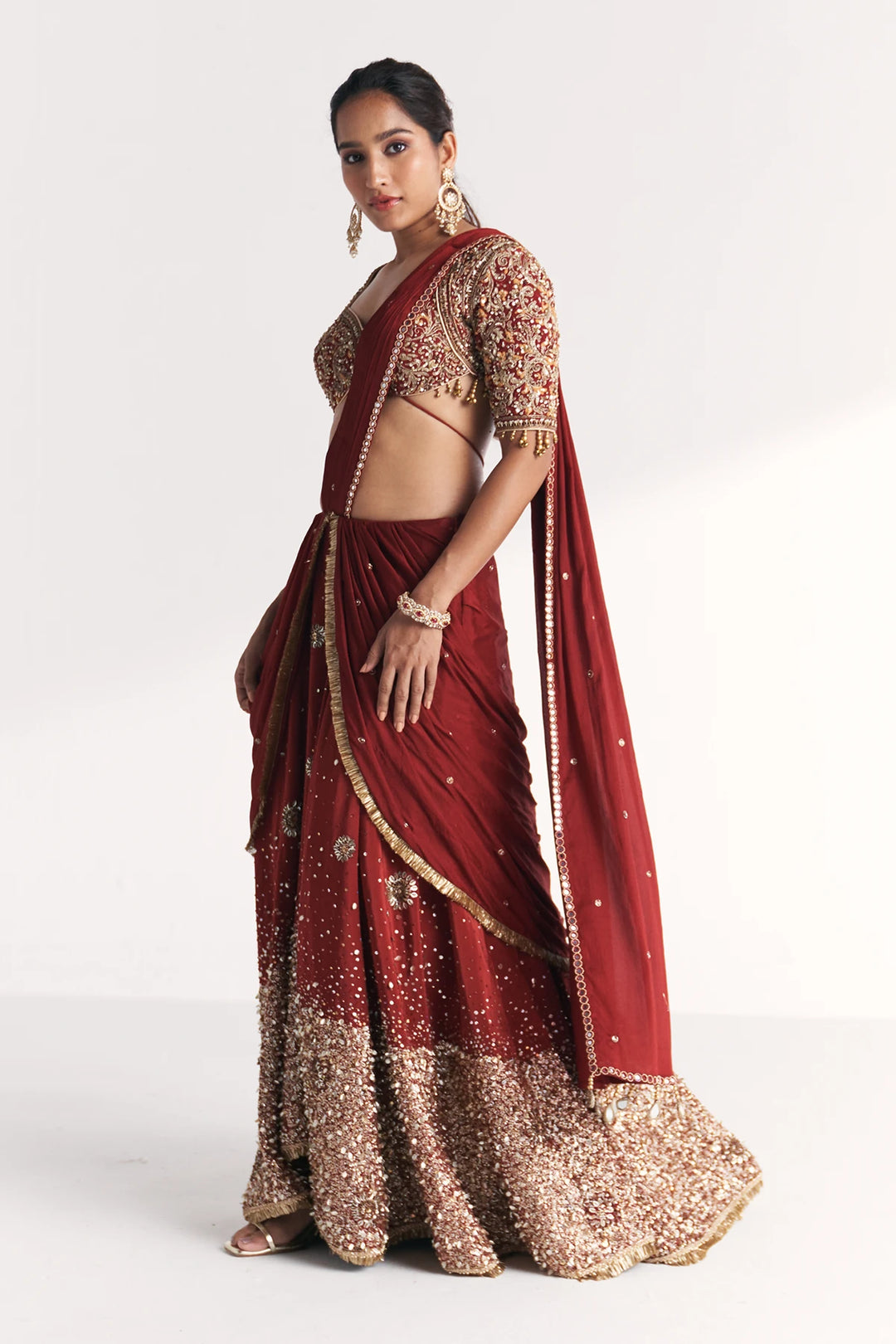Woman wearing a traditional maroon Saree with gold embroidery on a white background