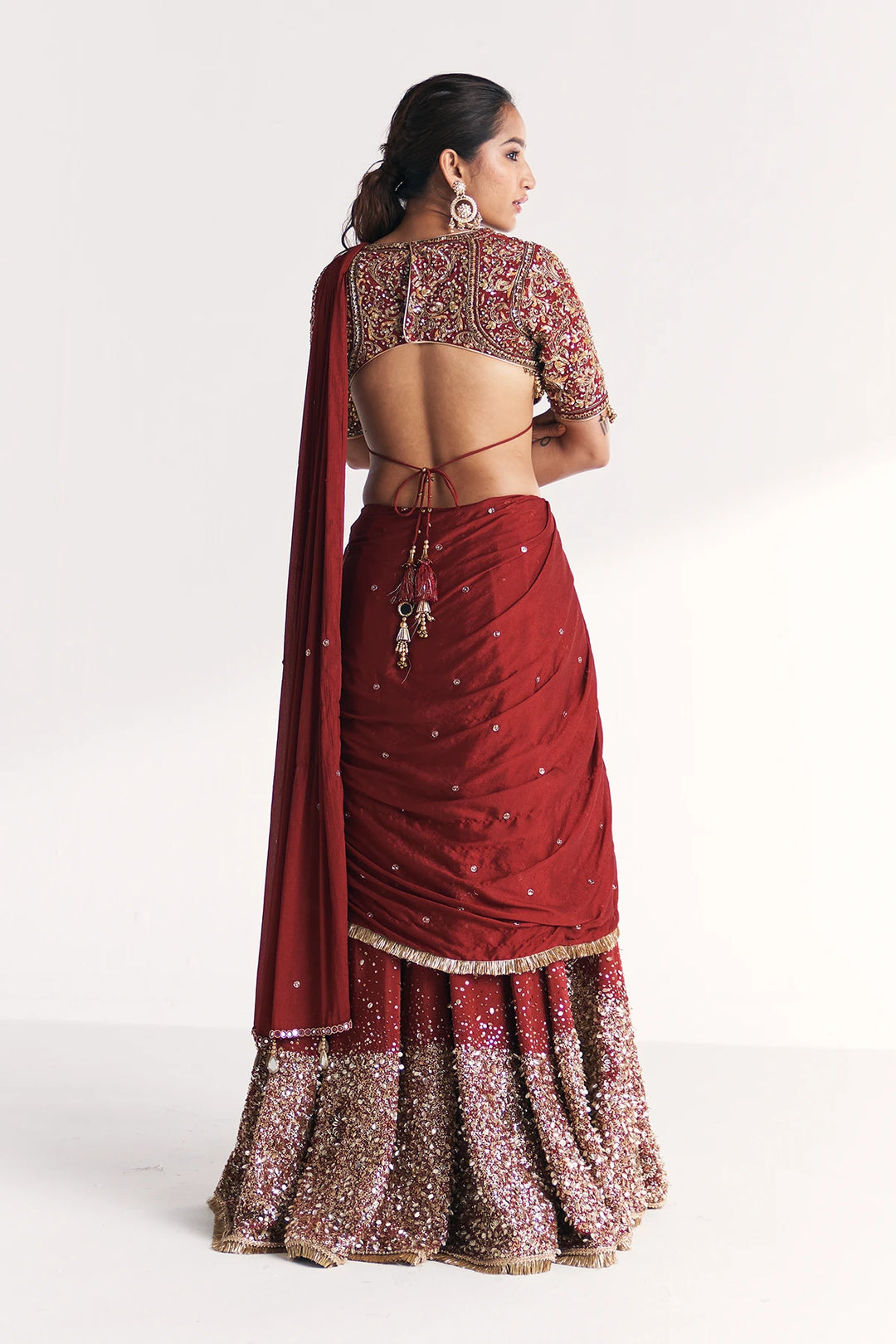Woman wearing a maroon saree with gold patterns on a white background