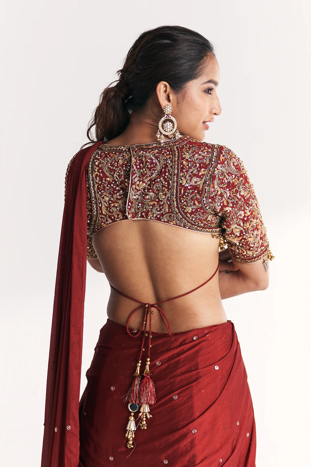 Woman wearing a red saree with intricate gold embroidery on a plain background