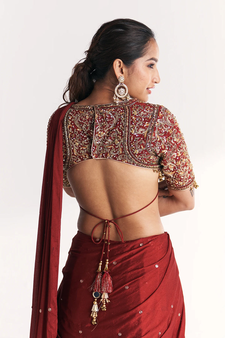 Woman wearing a red saree with intricate gold embroidery on a plain background