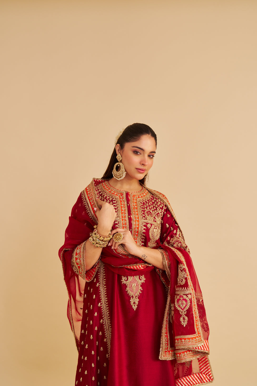 Woman wearing a red traditional Chauga with gold embroidery on a beige background
