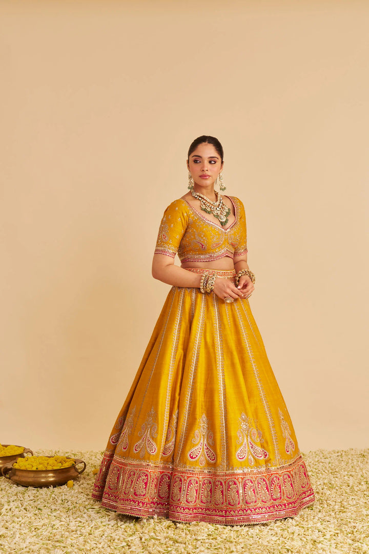 Woman wearing a yellow traditional lehenga with intricate designs on a beige background
