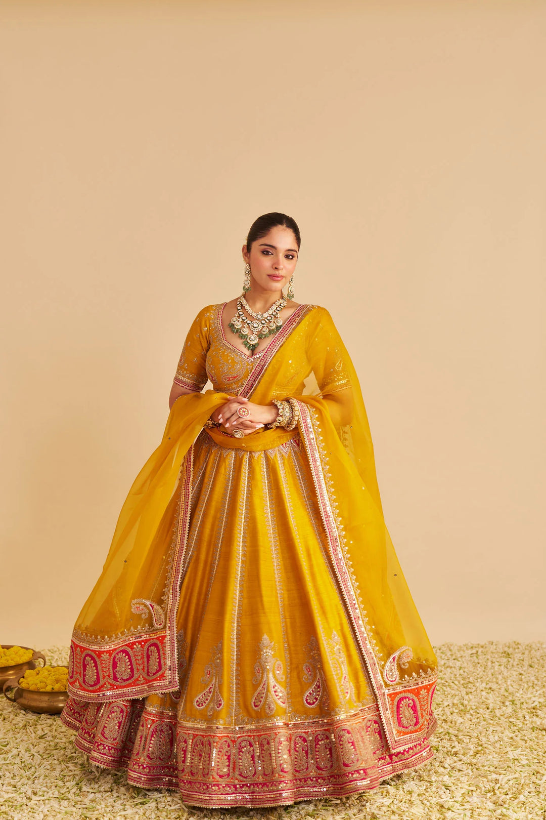 Woman in a yellow and red traditional lehenga with jewellery on a beige background