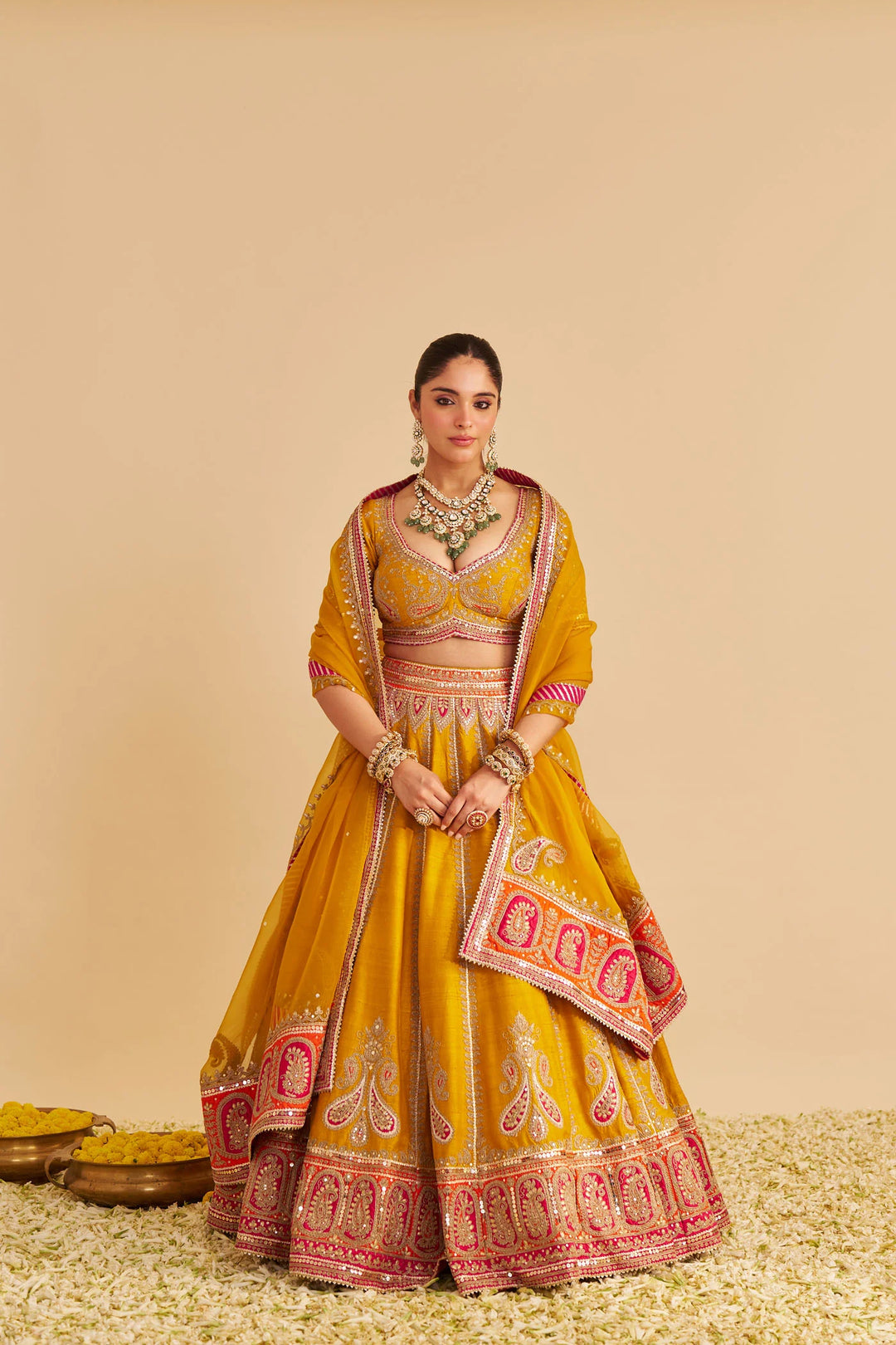 Woman in a yellow and red traditional lehenga with jewellery on a beige background