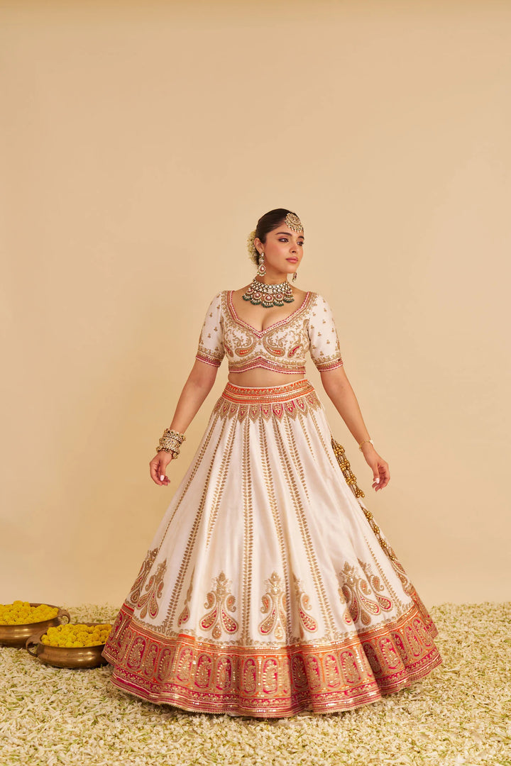 Woman wearing a traditional embroidered lehenga with a beige background