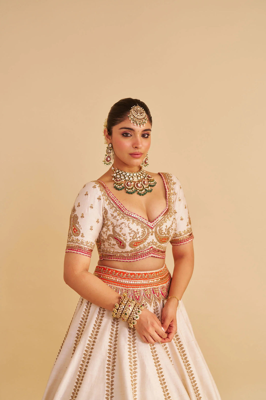 Woman wearing an embroidered traditional lehenga with jewelry on a beige background