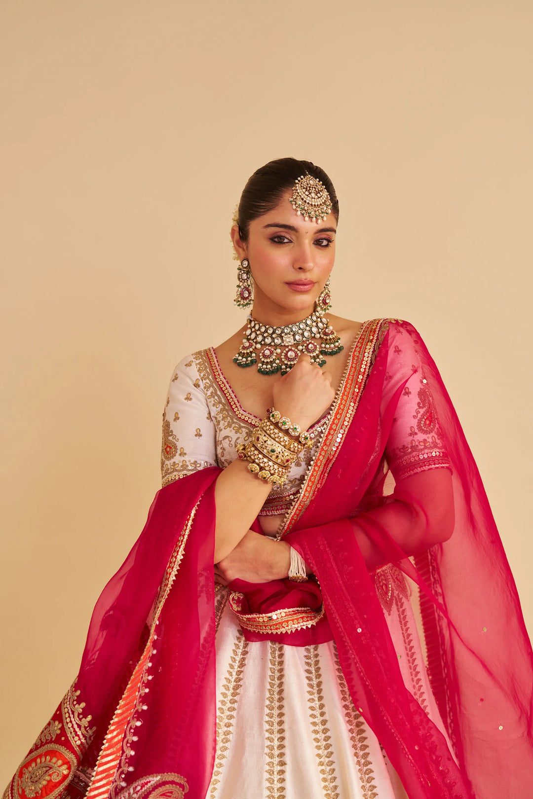 Woman in traditional Indian lehenga with jewelry against a beige background