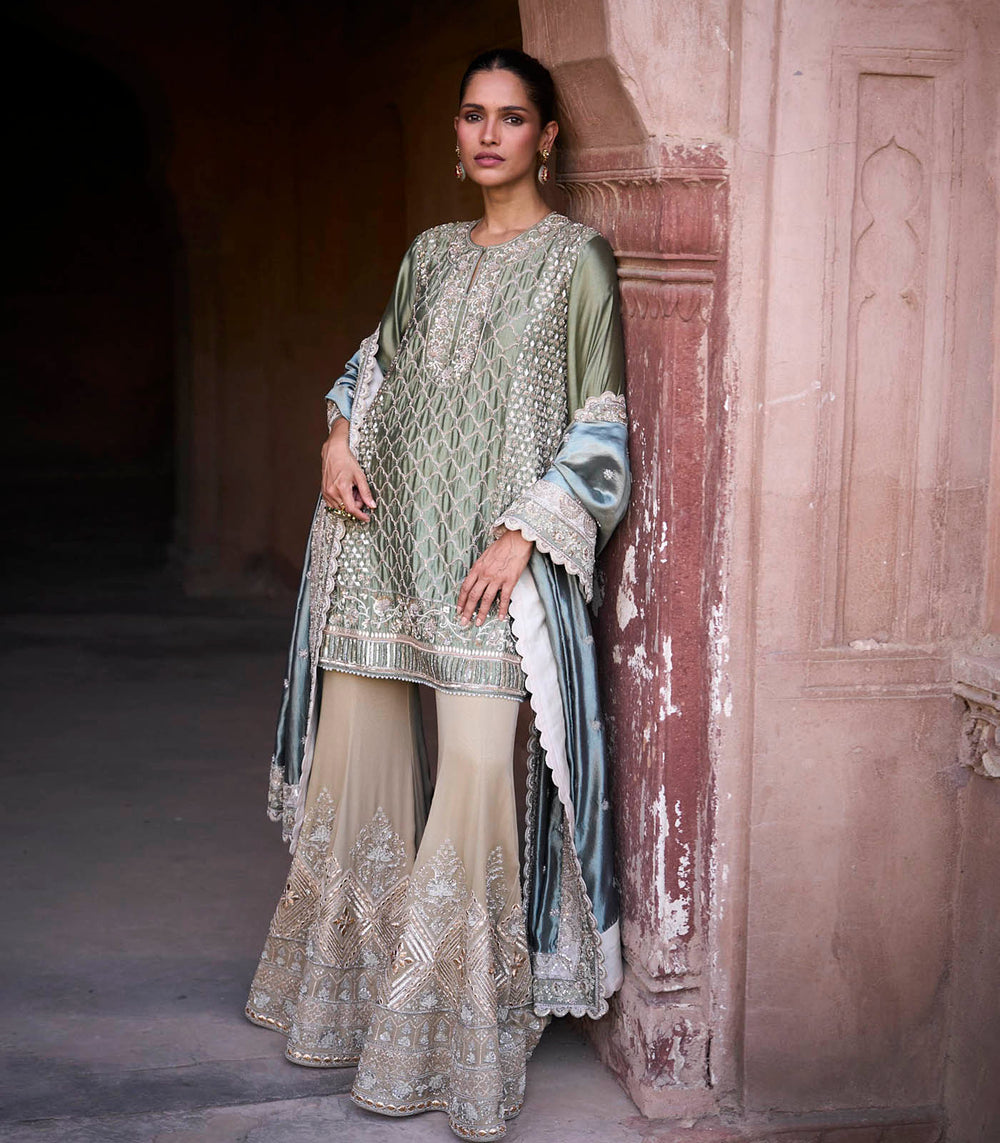Woman in traditional embroidered outfit standing against a textured wall.