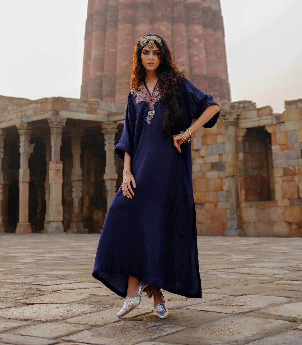 Woman in a long dark blue dress standing in front of stone architectural ruins.