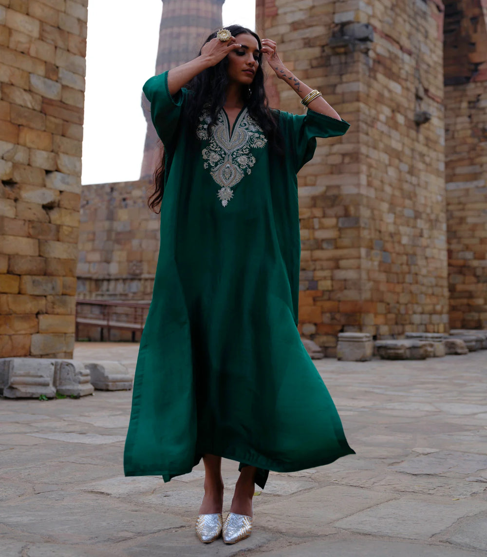 Woman in a green dress with white embroidery standing in front of stone ruins.