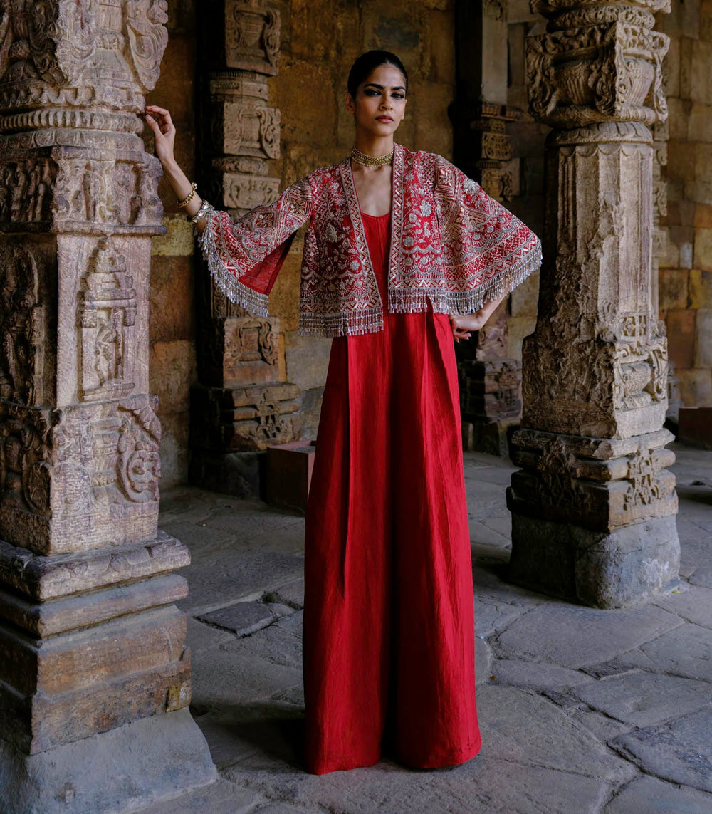 Woman in a red dress with a patterned shawl standing in an ancient stone setting.