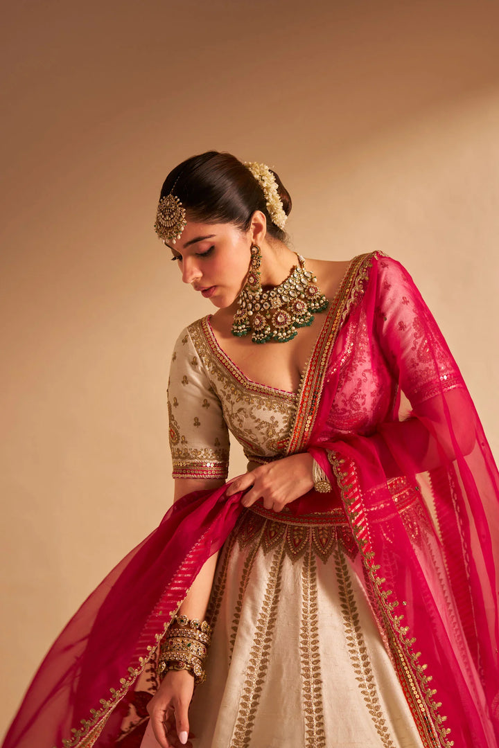 Woman in traditional Indian attire with a red dupatta and gold jewelry against a beige background
