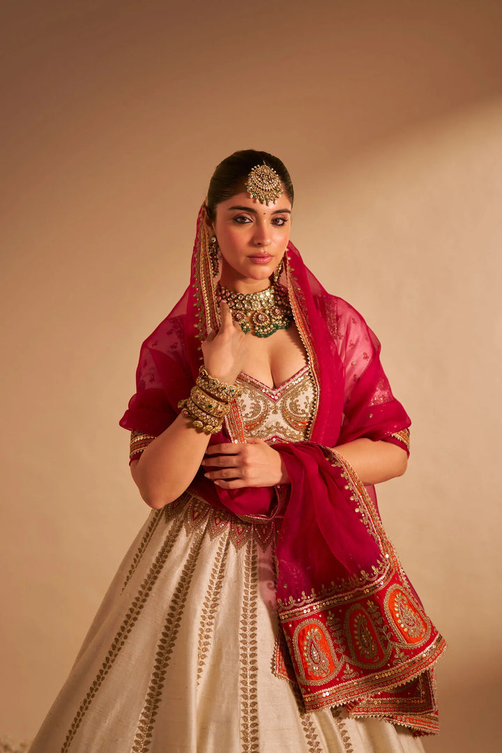 Woman in traditional Indian attire with a red dupatta against a beige background