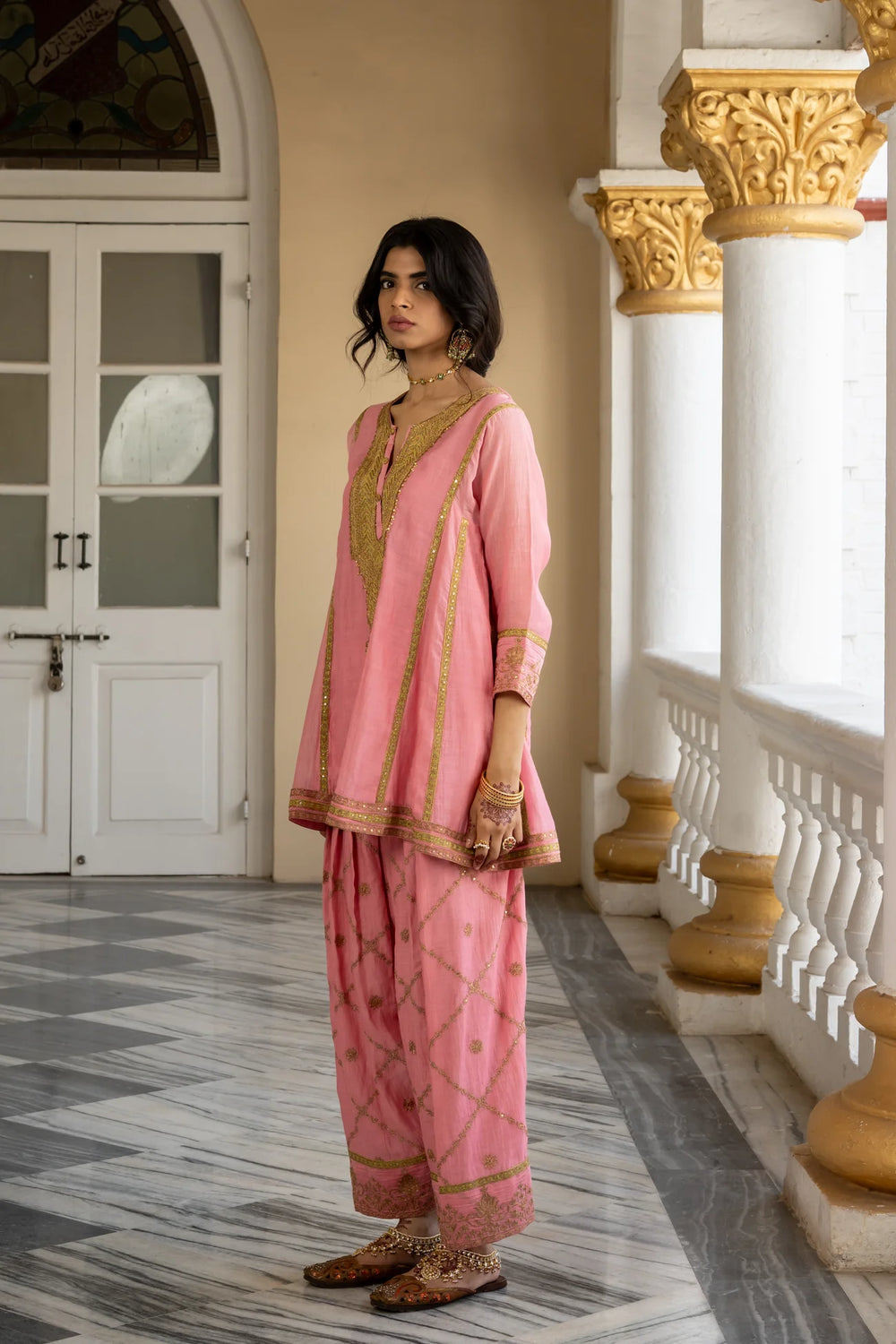 Woman in a pink traditional outfit standing in an elegant interior setting.