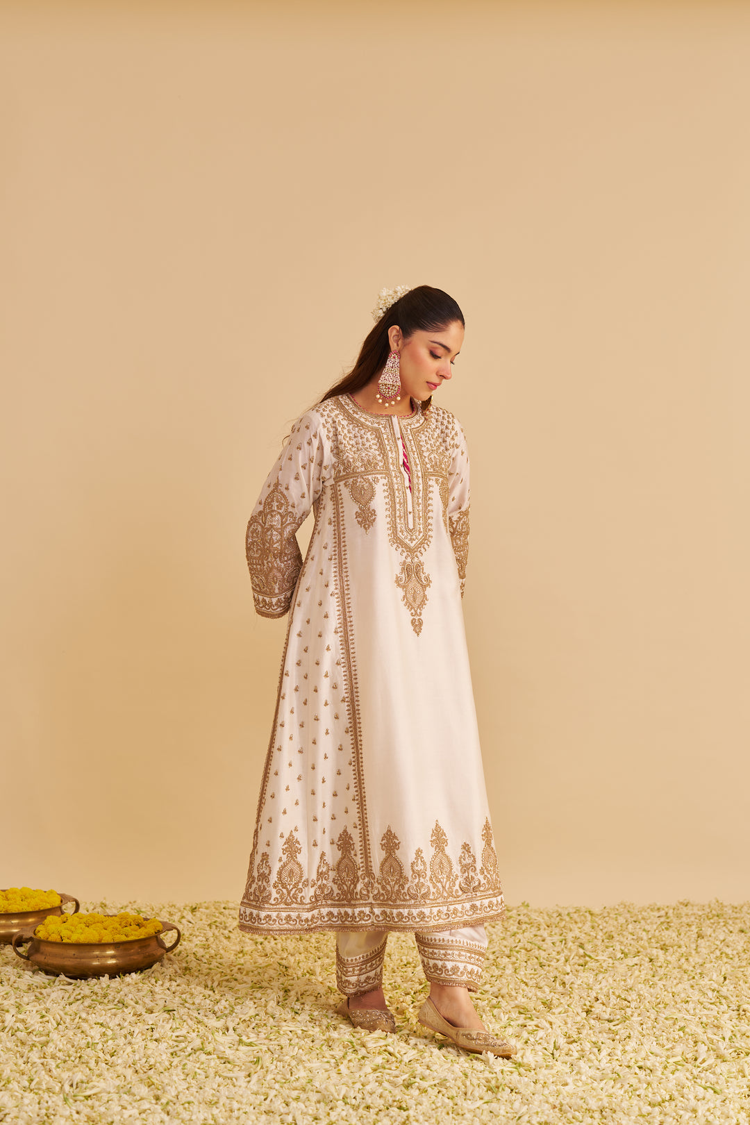 Woman in a white embroidered traditional Kurta standing on a beige background with decorative elements.