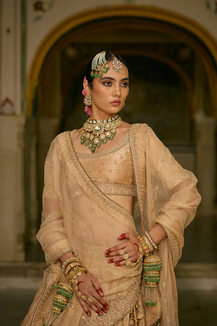 Woman in traditional beige lehenga with jewellery against a blurred architectural background