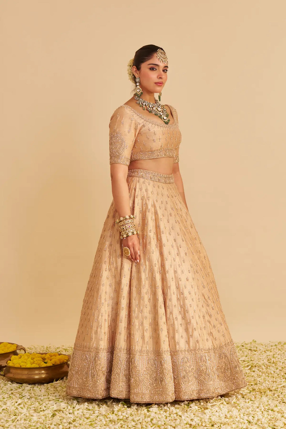 Woman wearing a traditional beige lehenga with jewellery against a beige background