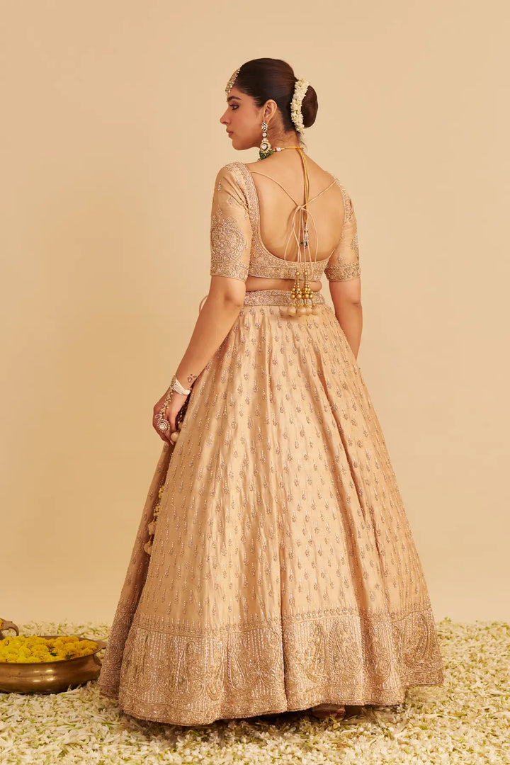 Woman wearing a beige embroidered traditional lehenga on a beige background