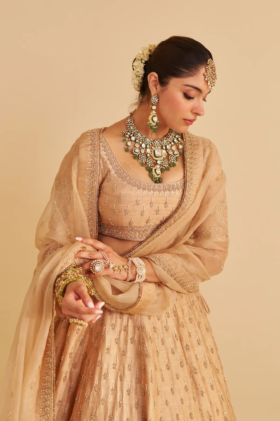 Woman in traditional beige lehenga with jewelry against a beige background