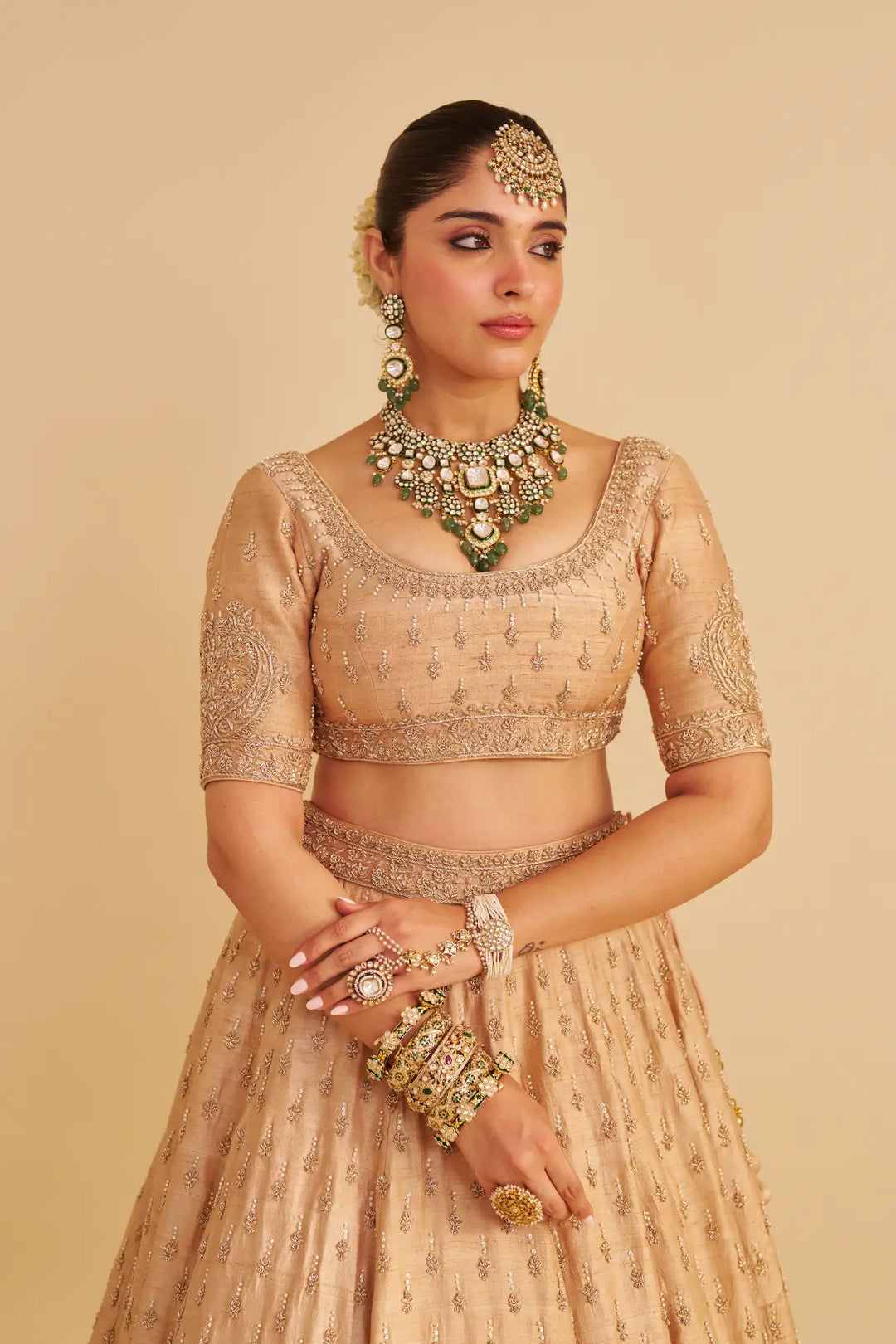 Woman in traditional beige embroidered lehenga with jewelry on a beige background